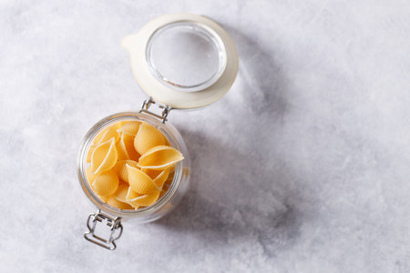 Raw uncooked dried Conchiglie shell pasta. Italian seashells pasta in jar on white background. Selective focusの写真素材
