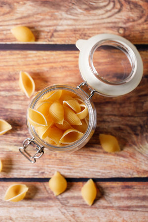 Raw uncooked dried Conchiglie shell pasta. Italian seashells pasta in jar on wooden background. Selective focusの写真素材