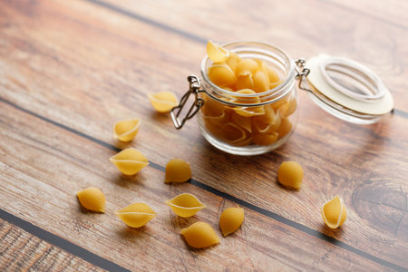 Raw uncooked dried Conchiglie shell pasta. Italian seashells pasta in jar on wooden background. Selective focusの写真素材
