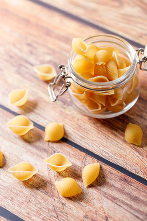 Raw uncooked dried Conchiglie shell pasta. Italian seashells pasta in lock lid jar on wooden background. Selective focusの写真素材