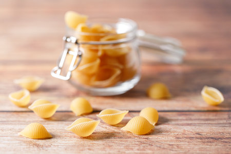 Raw uncooked dried Conchiglie shell pasta. Italian seashells pasta in lock lid jar on wooden background. Selective focusの写真素材