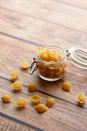 Raw uncooked dried Conchiglie shell pasta. Italian seashells pasta in lock lid jar on wooden background. Selective focusの写真素材