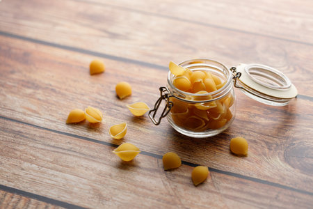 Raw uncooked dried Conchiglie shell pasta. Italian seashells pasta in lock lid jar on wooden background. Selective focusの写真素材