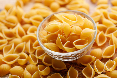 Raw uncooked dried Conchiglie shell pasta. Italian seashells pasta in glass bowl on wooden background. Selective focusの写真素材