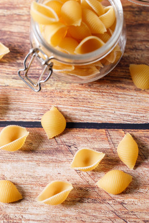 Raw uncooked dried Conchiglie shell pasta. Italian seashells pasta in jar on wooden background....