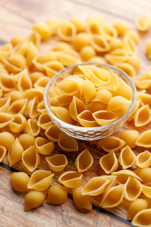 Raw uncooked dried Conchiglie shell pasta. Italian seashells pasta in glass bowl on wooden background. Selective focusの写真素材