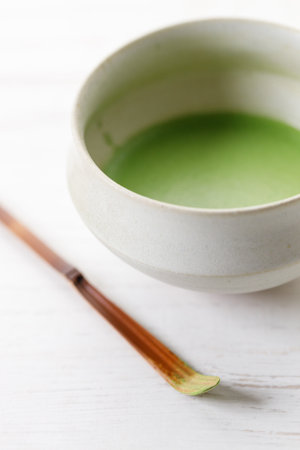Cup of fresh matcha tea, green tea and Chashaku or tea scoop, equipments for preparing matcha green tea, on white wooden table. Selective focus.の写真素材