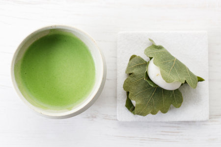 Kashiwa mochi and Cup of fresh matcha tea. Japanese sweet from mochi or rice cake and sweet red bean paste filling surrounded with Kashiwa or Oak leaf . Selective focus.の写真素材