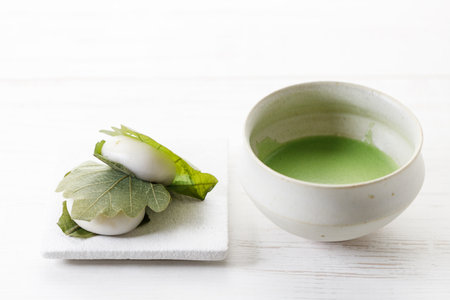 Kashiwa mochi and Cup of fresh matcha tea. Japanese sweet from mochi or rice cake and sweet red bean paste filling surrounded with Kashiwa or Oak leaf . Selective focus.の写真素材