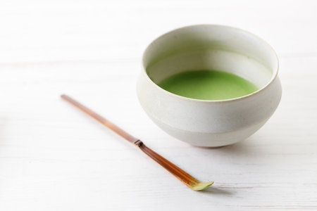 Cup of fresh matcha tea, green tea and Chashaku or tea scoop, equipments for preparing matcha green tea, on white wooden table. Selective focus.の写真素材