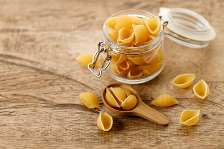 Raw uncooked dried Conchiglie shell pasta. Italian seashells pasta in glass jar on wooden background. Selective focusの写真素材