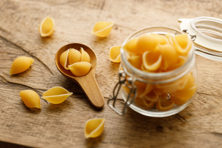 Raw uncooked dried Conchiglie shell pasta. Italian seashells pasta in lock lid glass jar on wooden background. Selective focusの写真素材