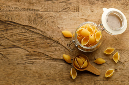 Raw uncooked dried Conchiglie shell pasta. Italian seashells pasta in glass jar on wooden background. Selective focusの写真素材