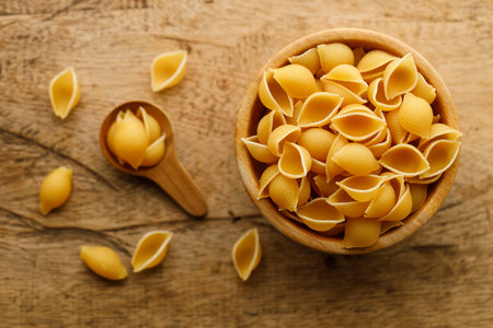 Raw uncooked dried Conchiglie shell pasta. Italian seashells pasta in wooden bowl on wooden background. Selective focusの写真素材
