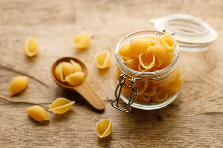Raw uncooked dried Conchiglie shell pasta. Italian seashells pasta in lock lid glass jar on wooden background. Selective focusの写真素材