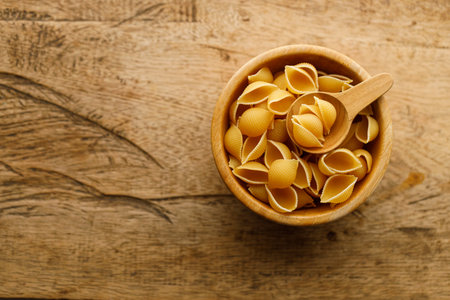 Raw uncooked dried Conchiglie shell pasta. Italian seashells pasta in wooden bowl on wooden background. Selective focusの写真素材