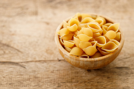 Raw uncooked dried Conchiglie shell pasta. Italian seashells pasta in wooden bowl on wooden background. Selective focusの写真素材