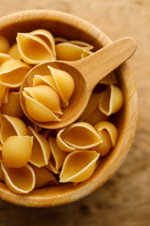 Raw uncooked dried Conchiglie shell pasta. Italian seashells pasta in wooden bowl on wooden background. Selective focusの写真素材