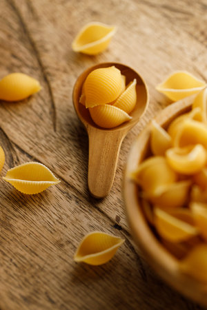 Raw uncooked dried Conchiglie shell pasta. Italian seashells pasta in wooden bowl on wooden background. Selective focusの写真素材