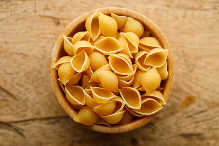 Raw uncooked dried Conchiglie shell pasta. Italian seashells pasta in wooden bowl on wooden background. Selective focusの写真素材