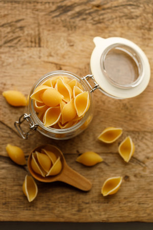 Raw uncooked dried Conchiglie shell pasta. Italian seashells pasta in lock lid glass jar on wooden background. Selective focusの写真素材