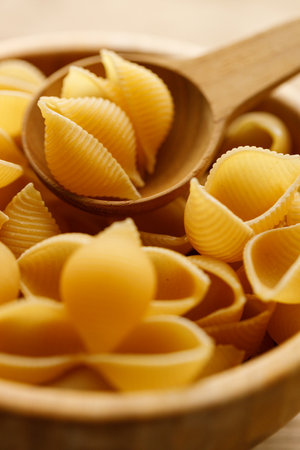 Raw uncooked dried Conchiglie shell pasta. Italian seashells pasta in wooden bowl on wooden background. Selective focusの写真素材