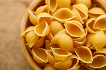 Raw uncooked dried Conchiglie shell pasta. Italian seashells pasta in wooden bowl on wooden background. Selective focusの写真素材