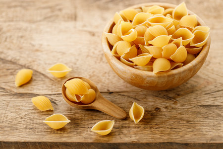 Raw uncooked dried Conchiglie shell pasta. Italian seashells pasta in wooden bowl on wooden background.の写真素材