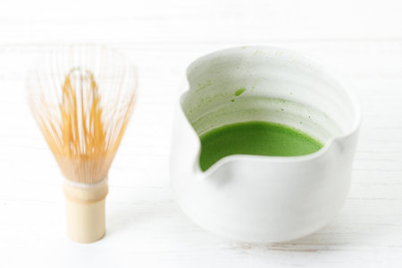 Cup of fresh matcha tea, green tea and Chasen, bamboo whisk, on white wooden table. Selective focus.の写真素材