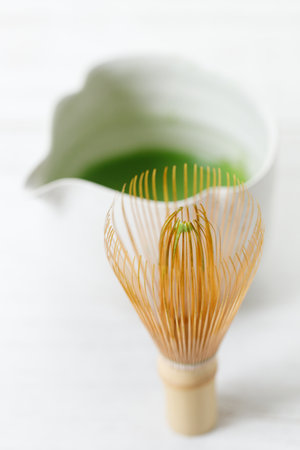 Cup of fresh matcha tea, green tea and Chasen, bamboo whisk, on white wooden table. Selective focus.の写真素材