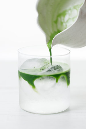 fresh matcha tea, green tea pouring on a glass of coconut water on white wooden table. Selective focus.の写真素材