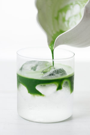 fresh matcha tea, green tea pouring on a glass of coconut water on white wooden table. Selective focus.の写真素材