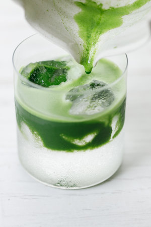 fresh matcha tea, green tea pouring on a glass of coconut water on white wooden table. Selective focus.の写真素材