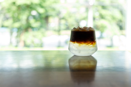 Cup of creation black coffee drink and coconut water decorated with coconut kernel on wooden table by the window. Selective focus.の写真素材