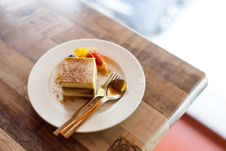 Freshly tiramisu cake on white ceramic plate decorated with fruit and edible flowers on wooden table background. Selective focus.の写真素材