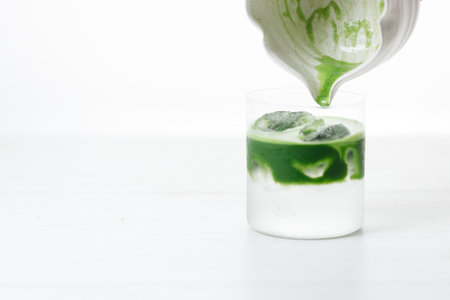fresh matcha tea, green tea pouring on a glass of coconut water on white wooden table. Selective focus.の写真素材
