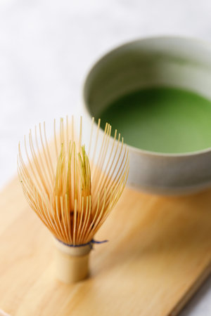 Cup of fresh matcha tea, green tea and Chasen, bamboo whisk, on wooden plate on white table. Selective focus.の写真素材