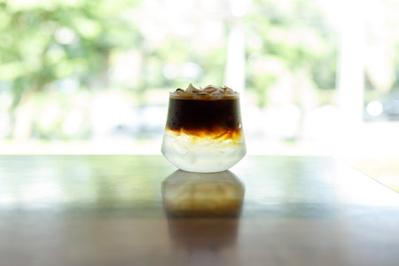 Cup of creation black coffee drink and coconut water decorated with coconut kernel on wooden table by the window. Selective focus.の写真素材