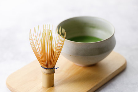 Cup of fresh matcha tea, green tea and Chasen, bamboo whisk, on wooden plate on white table. Selective focus.の写真素材