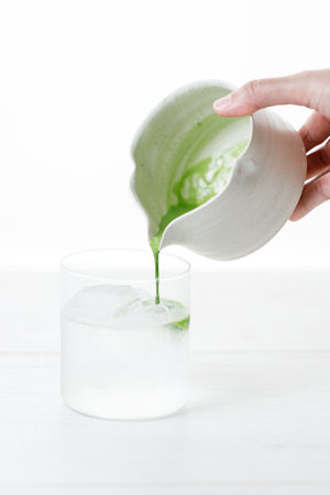 fresh matcha tea, green tea pouring on a glass of coconut water on white wooden table. Selective focus.の写真素材