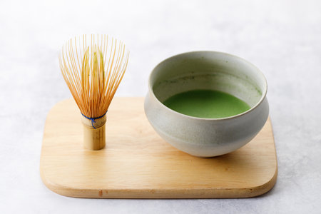 Cup of fresh matcha tea, green tea and Chasen, bamboo whisk, on wooden plate on white table. Selective focus.の写真素材