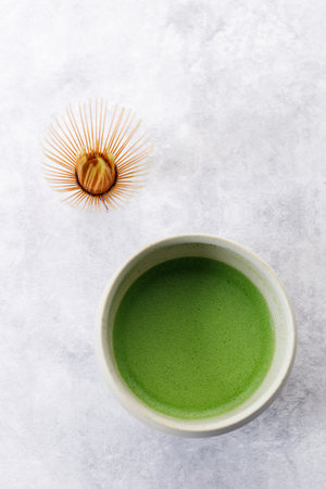 Cup of fresh matcha tea, green tea and Chasen, bamboo whisk, on wooden plate on white table. Selective focus.の写真素材