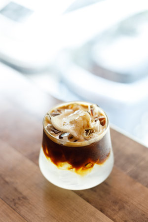 Cup of creation black coffee drink and coconut water decorated with coconut kernel on wooden table by the window. Selective focus.の写真素材