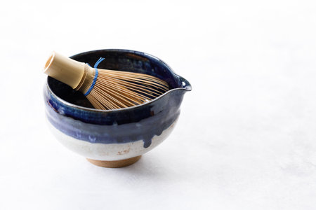 Japanese tea bowl glazed with blue and white color and Chasen or Bamboo whisk, an equipment for preparing matcha green tea on white wooden table. Selective focus.の写真素材