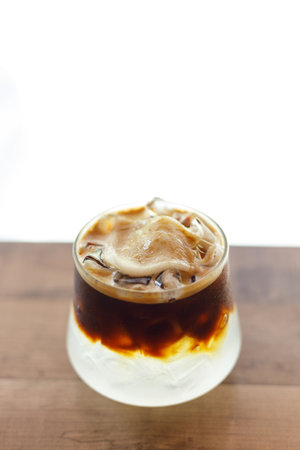 Cup of creation black coffee drink and coconut water decorated with coconut kernel on wooden table by the window. Selective focus.の写真素材