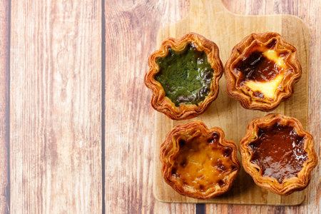 Stack of assorted Portuguese sweet dessert egg tart or Pastel de Nata on wooden board on wooden...