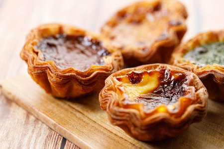 Stack of assorted Portuguese sweet dessert egg tart or Pastel de Nata on wooden board on wooden...