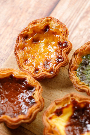 Stack of assorted Portuguese sweet dessert egg tart or Pastel de Nata on wooden board on wooden table.  Selective focus.の写真素材