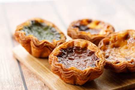 Stack of assorted Portuguese sweet dessert egg tart or Pastel de Nata on wooden board on wooden...
