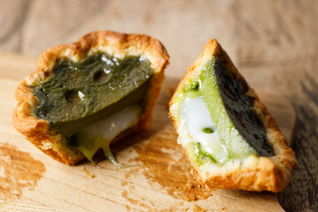 Closeup of Matcha and mochi Portuguese sweet dessert egg tart or Pastel de Nata on wooden board on wooden table.  Selective focus.の写真素材
